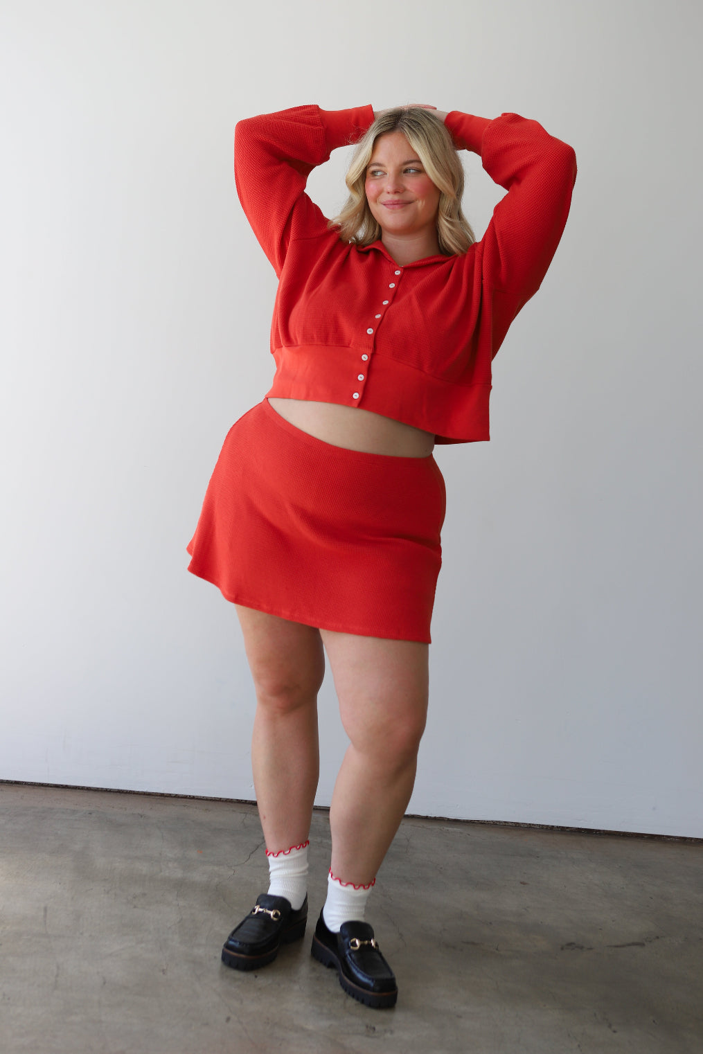 Woman wearing a paprika red outfit with a cropped cardigan and waffle skort against a white background