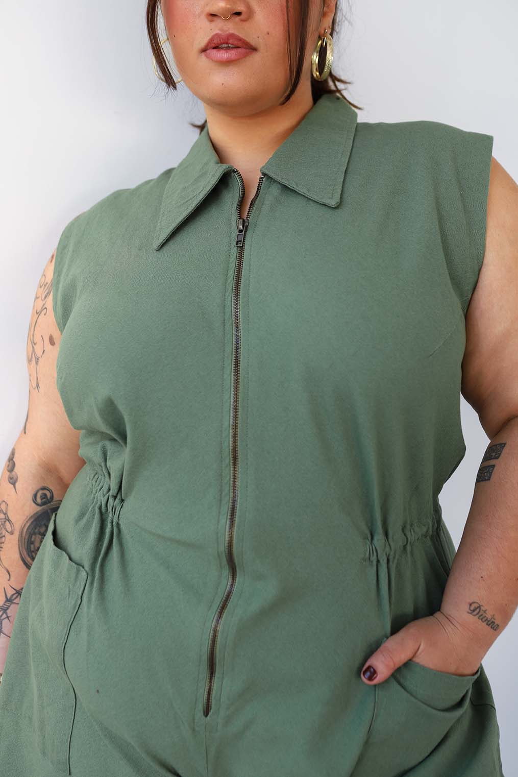 Person wearing a green sleeveless jumpsuit against a white background

